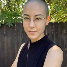 A color headshot of a person with very short hair, wearing glasses looking at the camera.
