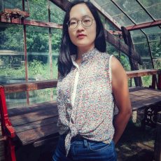 A color headshot of a person, who is wearing glasses and has shoulder length hair, looking at the camera.